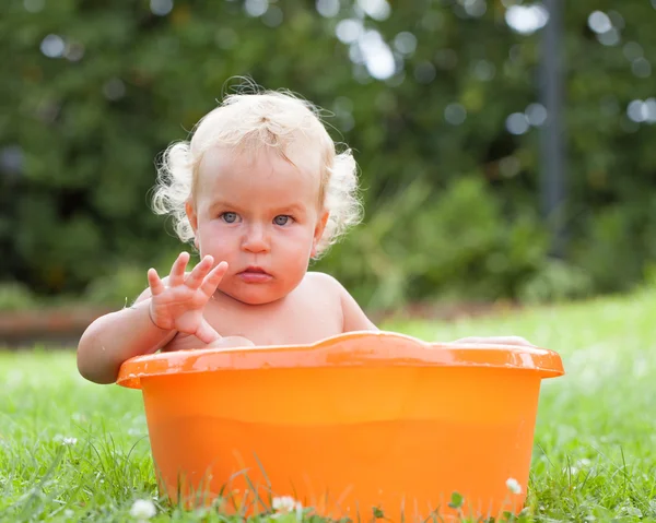 Pensive happy cute curly baby is bathed in orange pelvis — Stock Photo, Image