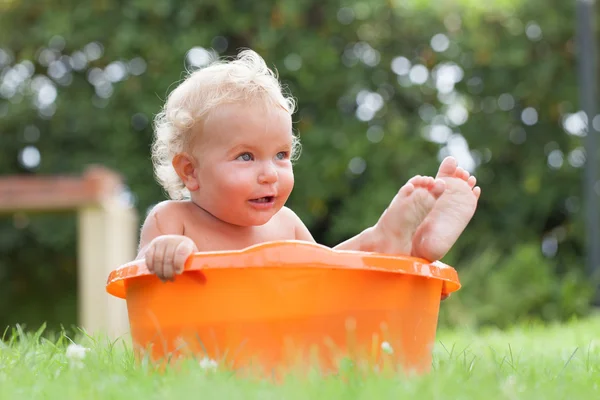 Alegre feliz lindo rizado bebé es bañado en naranja pelvis Imágenes De Stock Sin Royalties Gratis