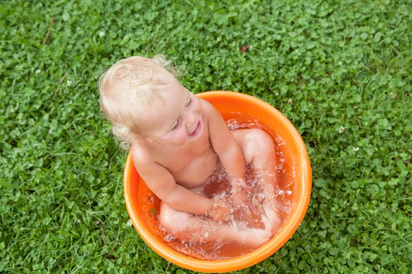 Fröhlich glücklich niedlich lockiges Baby ist in orangefarbenem Becken gebadet — Stockfoto