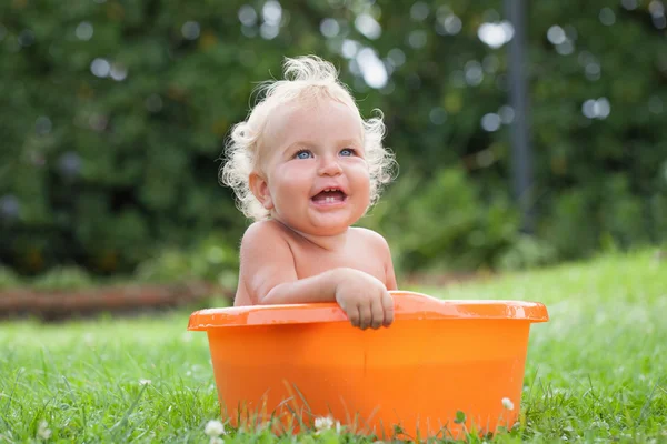 Веселий щасливий милий кучерявий дитина купається в помаранчевому таз — стокове фото