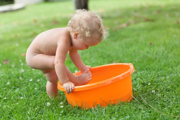 Pensativo feliz lindo rizado bebé es bañado en naranja pelvis — Foto de Stock