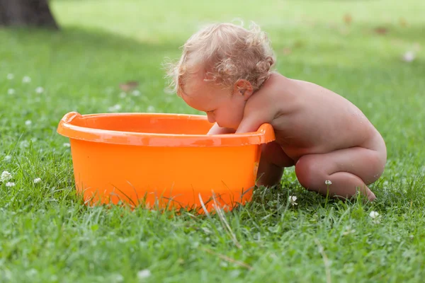 Pensativo feliz lindo rizado bebé es bañado en naranja pelvis — Foto de Stock