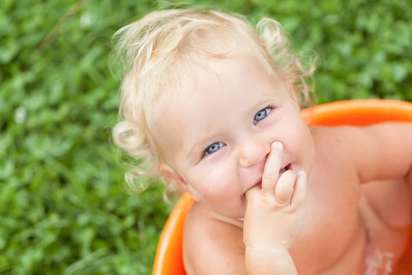 Cheerful happy cute curly baby is bathed in orange pelvis — Stock Photo, Image