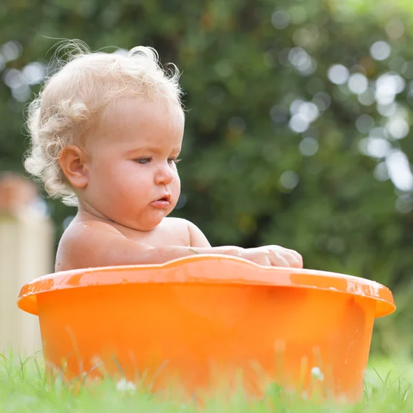 Bebê encaracolado bonito feliz pensativo é banhado em pelve laranja — Fotografia de Stock