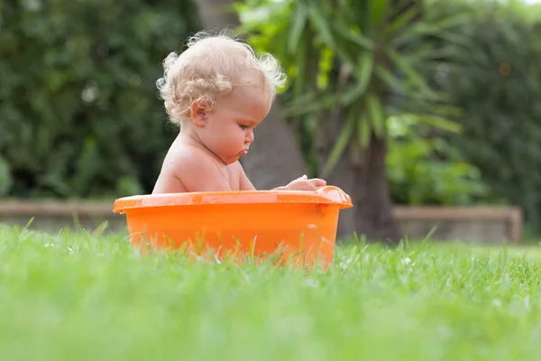 Pensativo feliz lindo rizado bebé es bañado en naranja pelvis — Foto de Stock