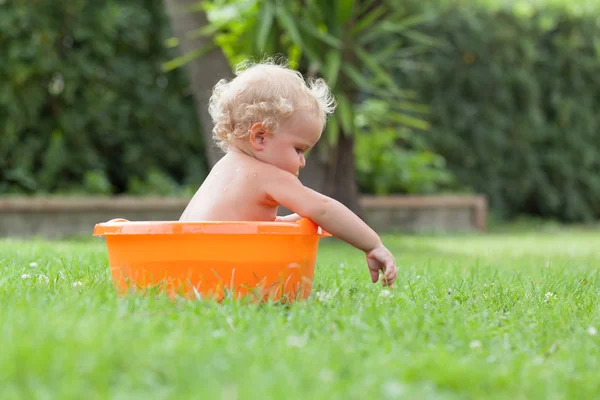 Bebê encaracolado bonito feliz pensativo é banhado em pelve laranja Imagem De Stock