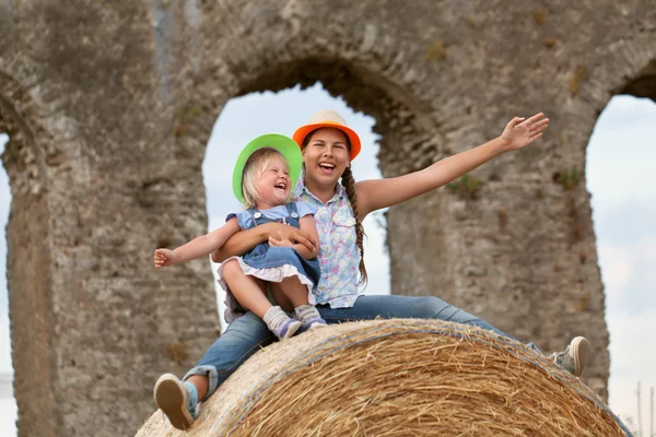 Portrait of happy cheerful sisters sitting on haystack — Stock Photo, Image