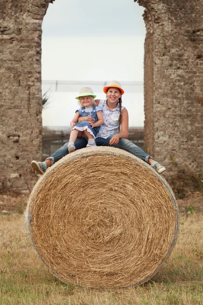 Portrait of happy cheerful sisters sitting on haystack — Stock Photo, Image