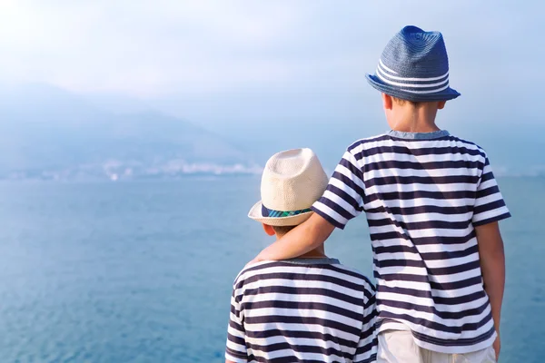Два брата обнимаются и смотрят на корабли, яхту на море — стоковое фото