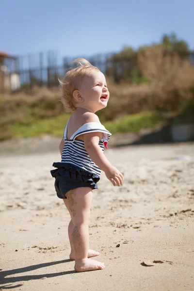 Happy cute girl in swimsuit playing with sand on beach — Stock Photo, Image