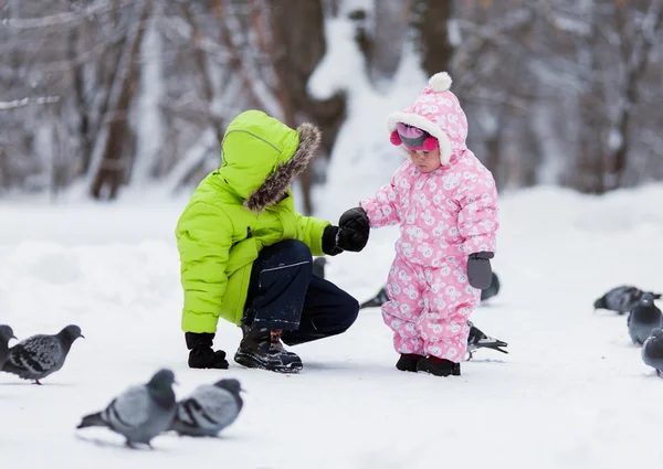 Little pretty girl and boy feed birds in winter snow park — Stock Photo, Image