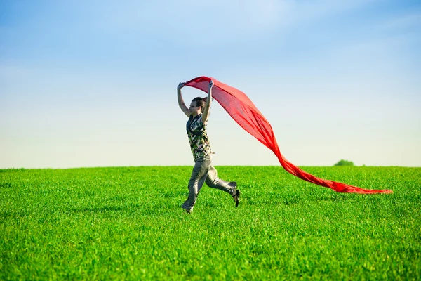 Beautiful young woman jumping on a green meadow with colored tissue — Stock Photo, Image