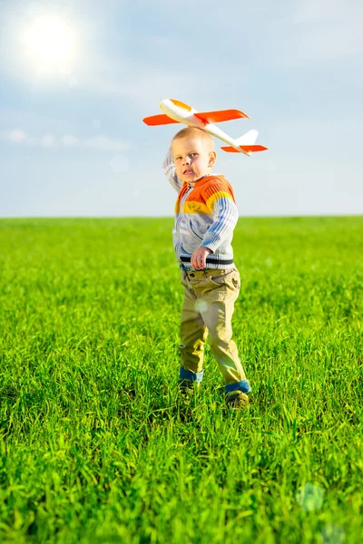 快乐的男孩玩玩具飞机攻击蓝色夏天天空和绿色领域背景. 免版税图库图片