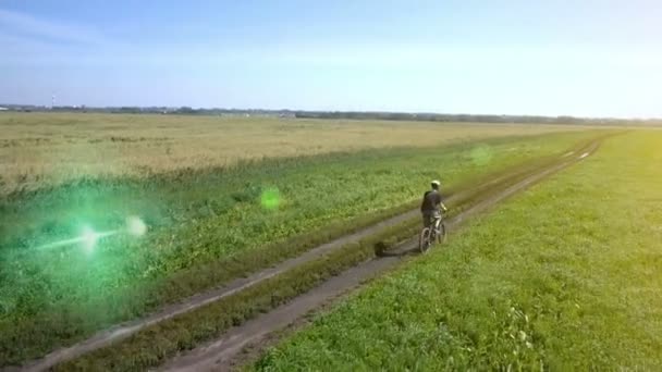 Anténa: Mladý muž na kole na kole na venkovské silnici přes zelené a žluté pole. — Stock video