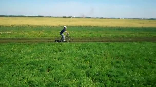 AERIAL: Joven ciclista en bicicleta en camino rural por campo verde y amarillo . — Vídeos de Stock