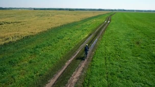 AEREO: Giovane in bicicletta su strada rurale attraverso il campo verde e giallo . — Video Stock