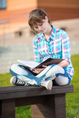 Öğrenci kızla defterini bankta. Yaz kampüs park.