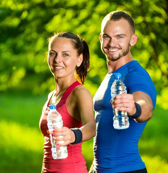 Pria dan wanita minum air dari botol setelah olahraga kebugaran — Stok Foto