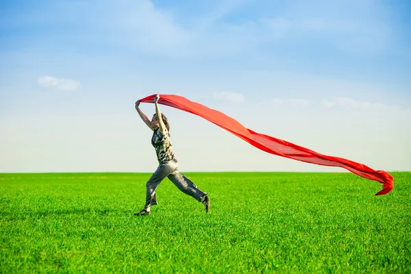 Hermosa mujer joven saltando en un prado verde con tejido de color — Foto de Stock