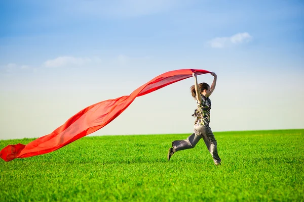 Beautiful young woman jumping on a green meadow with colored tissue — Stock Photo, Image