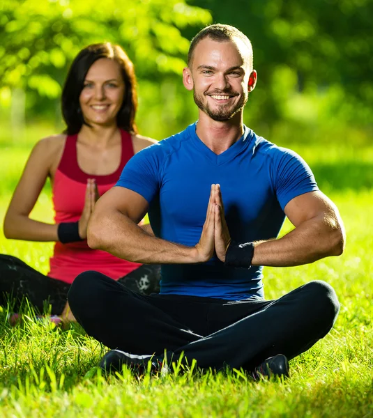 Genç adam ve kadın güneşli yaz parkta yoga yaparken — Stok fotoğraf