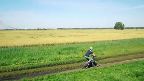 AEREO: Giovane in bicicletta su strada rurale attraverso il campo verde e giallo . — Video Stock