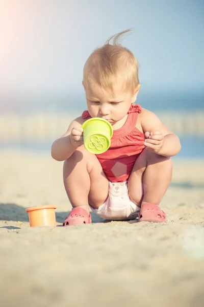 Bambina in abito rosso che gioca sulla spiaggia di sabbia vicino al mare . — Foto Stock