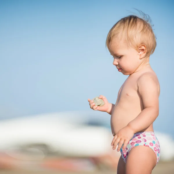 Schattige baby spelen met speelgoed aan zandstrand in de buurt van de zee. — Stockfoto