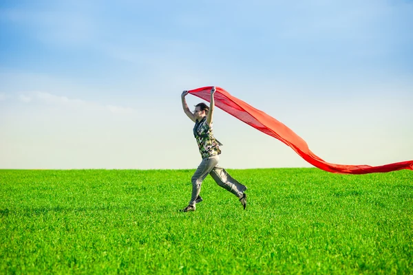 Belle jeune femme sautant sur une prairie verte avec des tissus colorés — Photo
