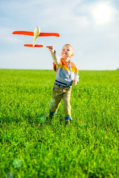 Happy boy playing with toy airplane against blue summer sky and green field background. — Stock Photo, Image