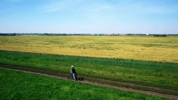 Anténa: Mladý muž na kole na kole na venkovské silnici přes zelené a žluté pole. — Stock video