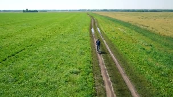 Antena: Młody człowiek na rowerze na rowerze na wiejskiej drodze poprzez zielone i żółte pola. — Wideo stockowe