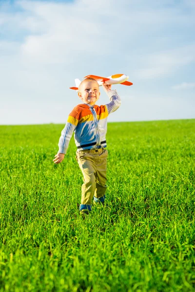 Happy boy playing with toy airplane against blue summer sky and green field background. — Stock Photo, Image