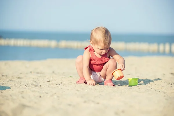 Bambina in abito rosso che gioca sulla spiaggia di sabbia vicino al mare . — Foto Stock