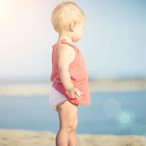 Mädchen im roten Kleid spielt am Sandstrand am Meer. — Stockfoto