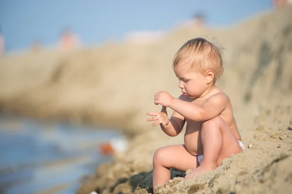 Bebê bonito brincando com brinquedos na praia de areia perto do mar . — Fotografia de Stock