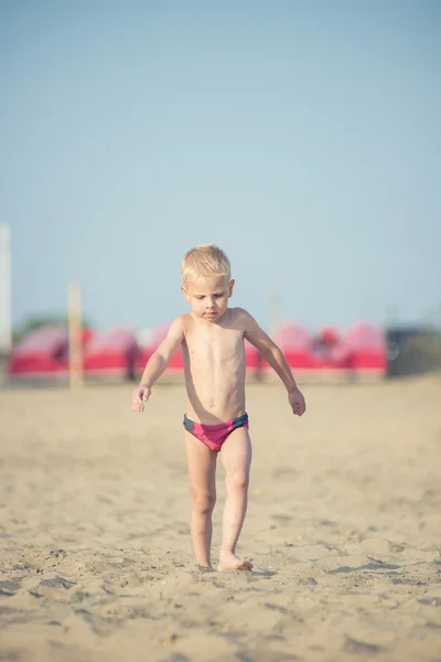 Ładny chłopczyk chodzenie na piaszczystej plaży w pobliżu morza. Na wybrzeżu Oceanu. — Zdjęcie stockowe