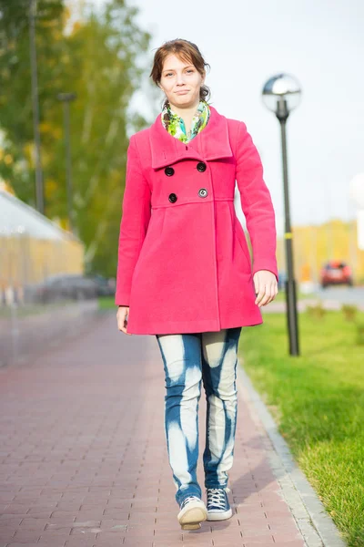 Schöne Frau in rotem Mantel geht herbstliche Straße. — Stockfoto