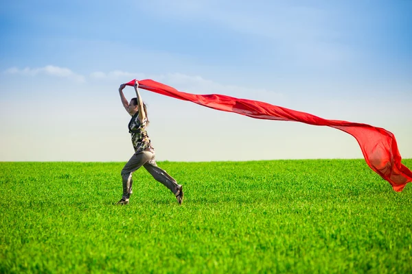 Belle jeune femme sautant sur une prairie verte avec des tissus colorés — Photo