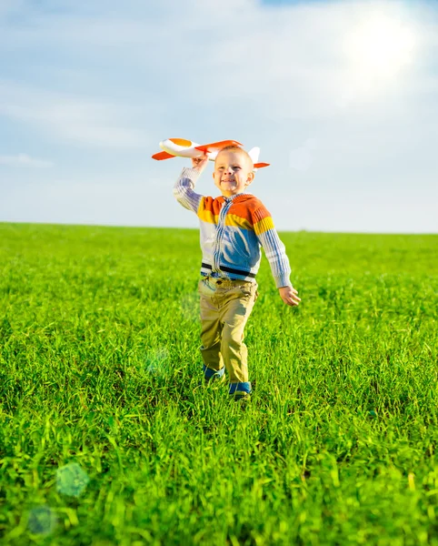 Счастливый мальчик играет с игрушечным самолетом на фоне голубого летнего неба и зеленого поля . — стоковое фото