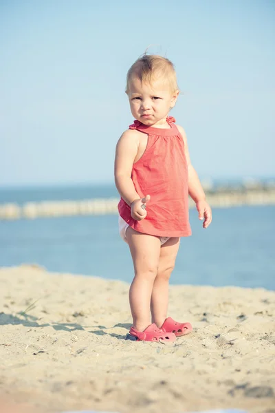 Menina bebê em vestido vermelho jogando na praia de areia perto do mar . — Fotografia de Stock