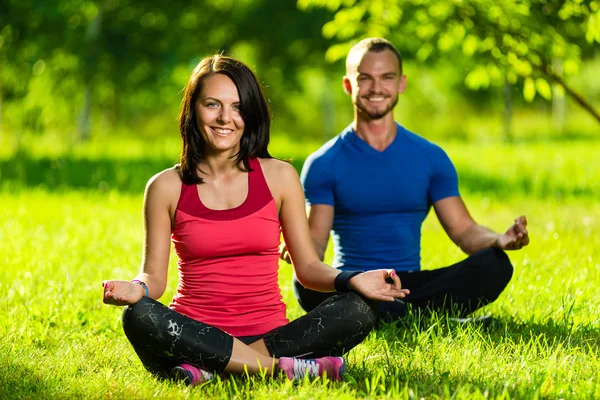 Young man and woman doing yoga in the sunny summer park — Stock Photo, Image