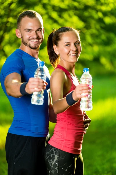 Uomo e donna che bevono acqua dalla bottiglia dopo l'esercizio fisico — Foto Stock