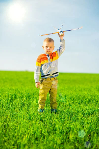 Niño feliz jugando con el avión de juguete contra el cielo azul de verano y el fondo verde del campo . — Foto de Stock