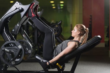 Bacaklar için ağırlıklar basın makine kullanan sportif kadın. Spor salonu.