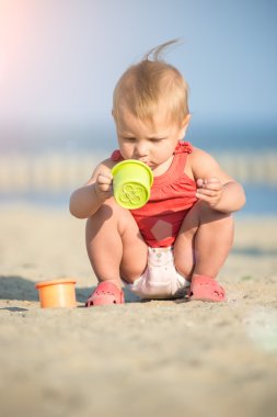 Denize yakın kumlu plajda oynayan Kırmızı elbiseli kız bebek.
