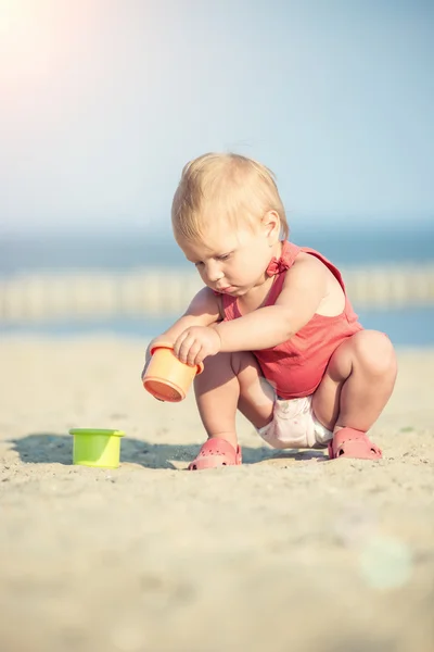 Bambina in abito rosso che gioca sulla spiaggia di sabbia vicino al mare . — Foto Stock