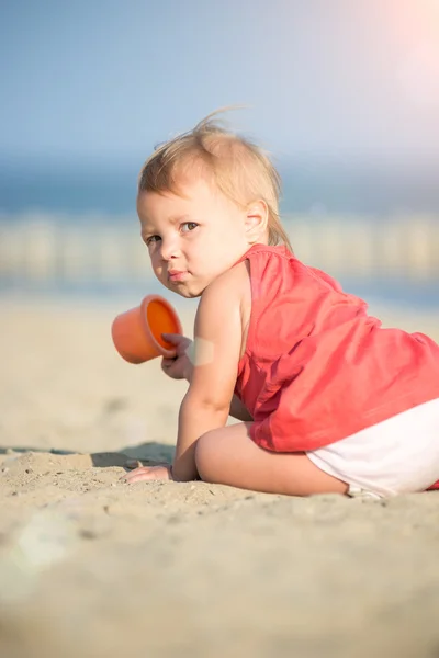 Dziewczynka w czerwonej sukience grając na piaszczystej plaży w pobliżu morza. — Zdjęcie stockowe