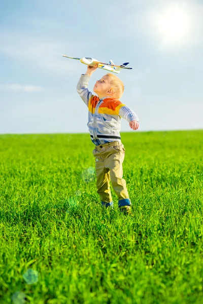 快乐的男孩玩玩具飞机攻击蓝色夏天天空和绿色领域背景. — 图库照片