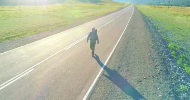 Asfalt yolda yürüyen otostopçu turist üzerinden uçuş. Yaz günü büyük bir kırsal vadi. Sırt çantalı gezgin..